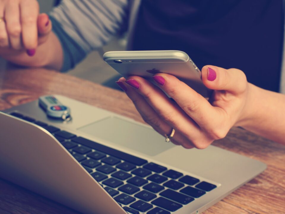 Person using smartphone and laptop simultaneously at a desk.
